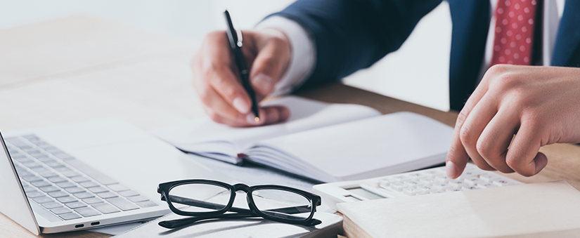 Corretor 2.0:corretor escreve em caderno enquanto com o laptop a sua frente