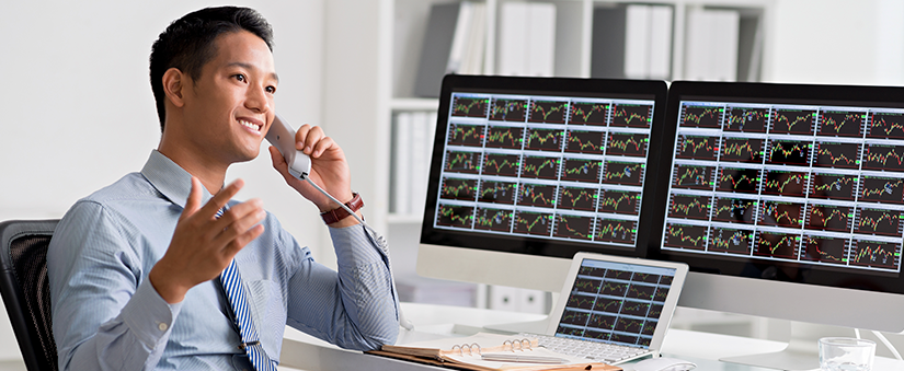 Vender mais imóveis: consultor falando ao telefone enquanto dois monitores de computador apresentam dezenas de gráficos