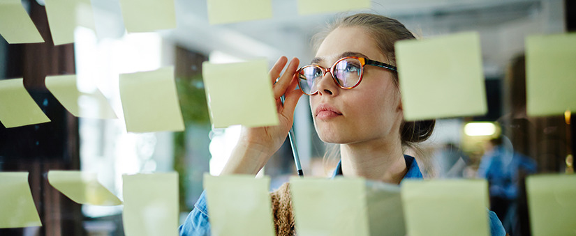 Mapeamento do processo de vendas: colaboradora olha pensativa para post its colados em parede de vidro