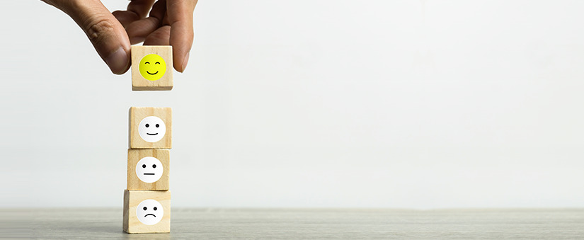 Mão apoiando blocos de madeira com as carinhas da mais triste à mais feliz