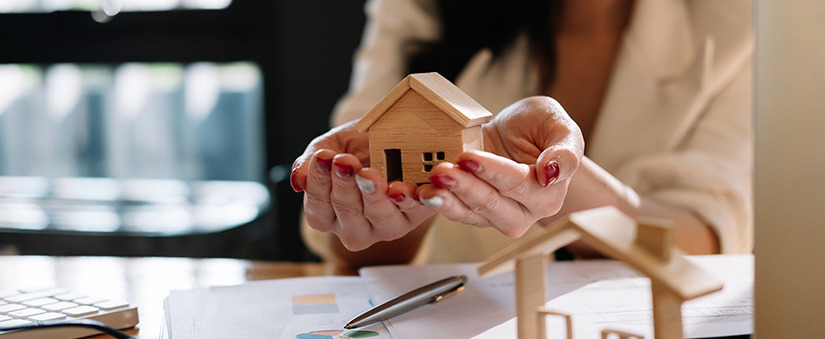 close nas mãos de uma mulher segurando uma casa de madeira em miniatura