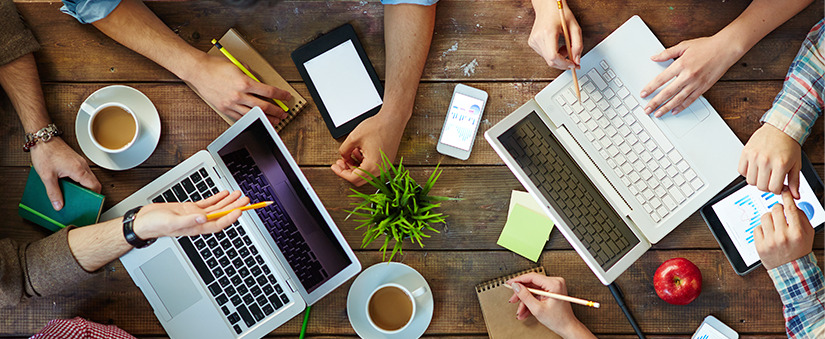 omnicanal mesa vista de cima com recorte de mãos, notebooks, canetas, celulares, papeis, etc.