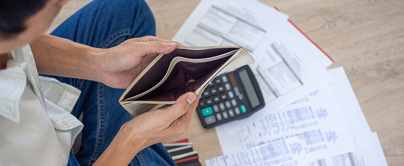 dicas para economizar dinheiro imagem vista de cima. Um homem abre uma carteira vazia. No chão alguns papeis espalhados.