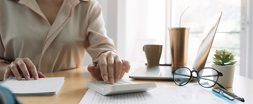gestão eficiente gestão eficiente: close nua mesa com alguns papeis espalhados, notebook, óculos, itens de escritório e uma mão manuseando uma calculadora.
