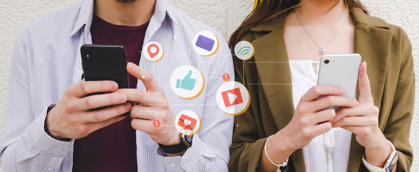 como ser bem-sucedido no mercado imobiliário close nas mãos de duas pessoas lado a lado segurando celulares. Entre as duas alguns ícones que representam redes sociais.