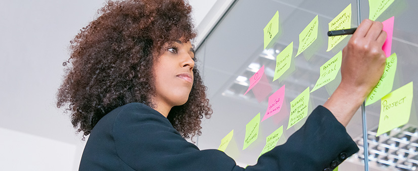 Ferramentas de Produtividade Ferramentas de Produtividade: mulher escrevendo em post it numa parede de vidro.