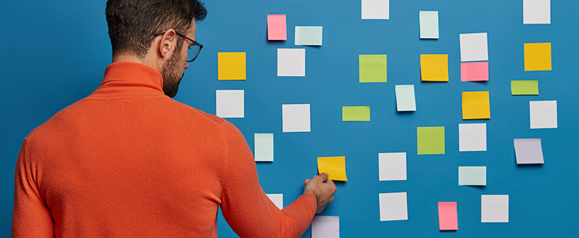 como gerenciar melhor meu tempo homem de costas colando post-its coloridos na parede.