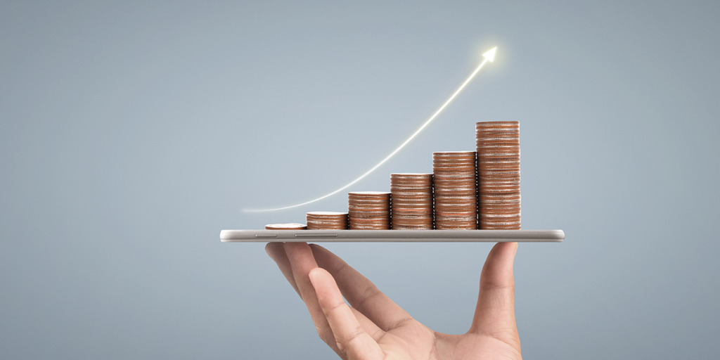 adimplência adimplência: imagem de uma mão segurando um celular com algumas moedas empilhadas.