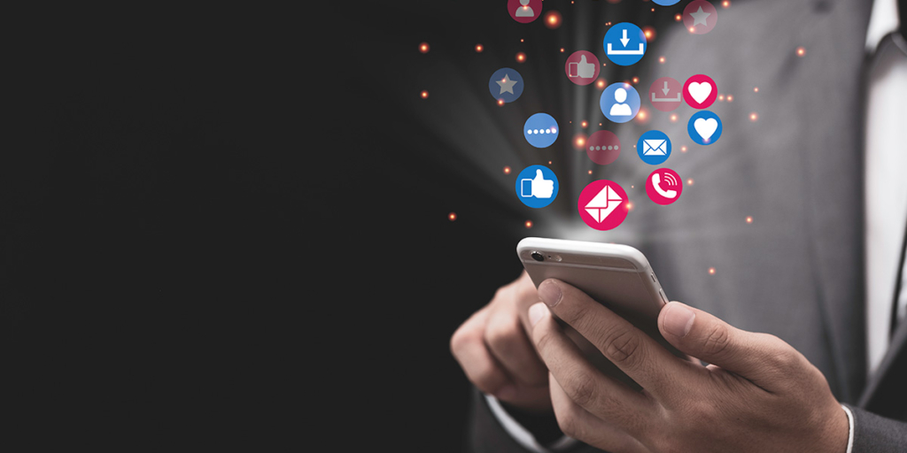 tecnologia persuasiva tecnologia persuasiva: close nas mãos de uma pessoa segurando um celular e, saindo da tela, alguns ícones que representam interações na internet.