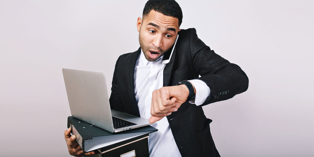 Dicas para corretor de imóveis iniciante Dicas para corretor de imóveis iniciante: homem com expressão de surpresa olhando para um relógio no pulso e segurando pastas, notebook e falando ao celular.