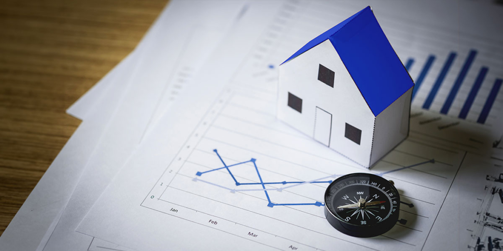 compra de imóveis: imagem de uma mesa vista de cima de vários papeis com gráficos e uma miniatura de casa.