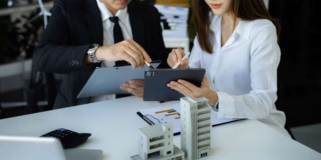O que é permuta de imóveis: duas pessoas segurando tablets e apontando canetas para um deles.