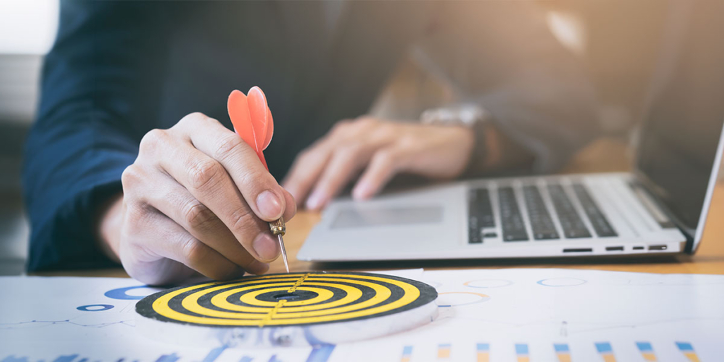 Jornada de compra: close numa mão colocando um dardo no meio de uma placa com alvo.