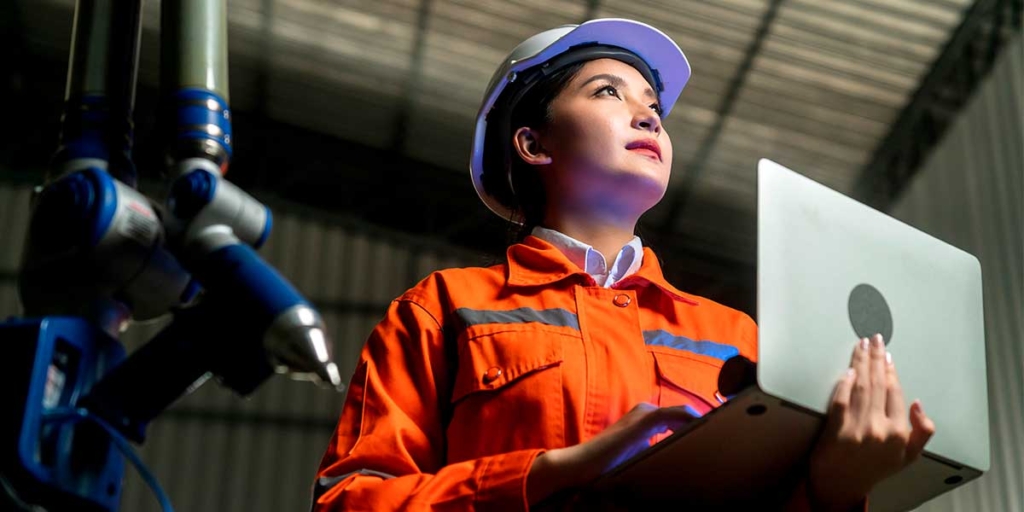 Notícias da Construção Civil Notícias da Construção Civil: imagem de uma mulher usando EPIs, com um notebook nas mãos.