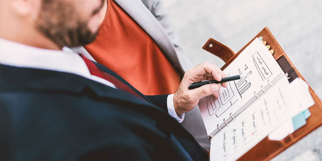 Script para corretor de imóveis: homem mostrando para uma pessoa ao lado um papel com esboço de gráfico.