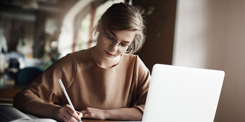 Script para corretor de imóveis Script para corretor de imóveis: mulher escrevendo num papel em frente a um notebook.