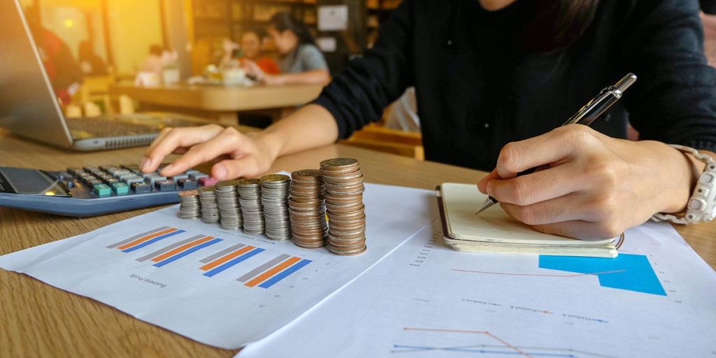 Contas a receber Contas a receber: close nas mãos de uma mulher numa mesa escrevendo num caderno e segurando uma calculadora.