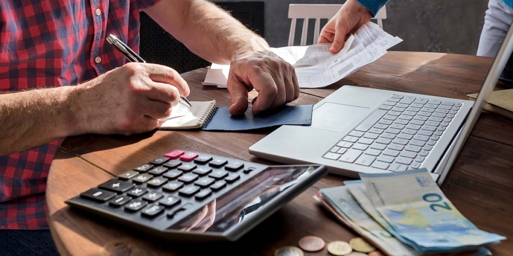 Contas a receber Contas a receber: close nas mãos de pessoas segurando papeis numa mesa com algumas cédulas de dinheiro, uma calculadora e um notebook.
