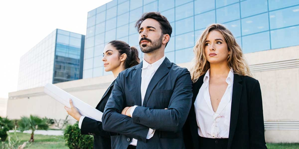 Mercado imobiliário de alto padrão Mercado imobiliário de alto padrão: imagem de três pessoas usando terno em frente a alguns prédios espelhados.