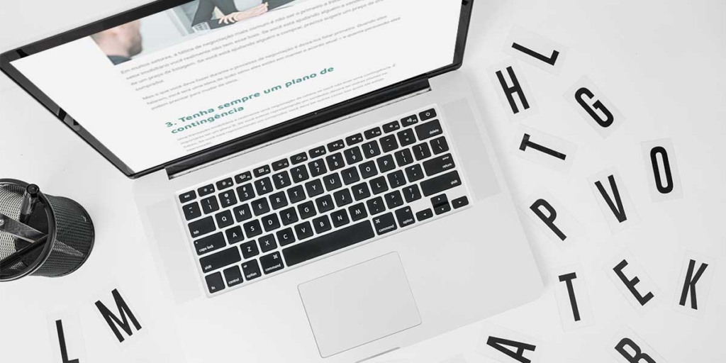 Palavras que despertam interesse Palavras que despertam interesse: imagem de uma mesa vista de cima com um notebook e algumas letras espalhadas pela mesa.