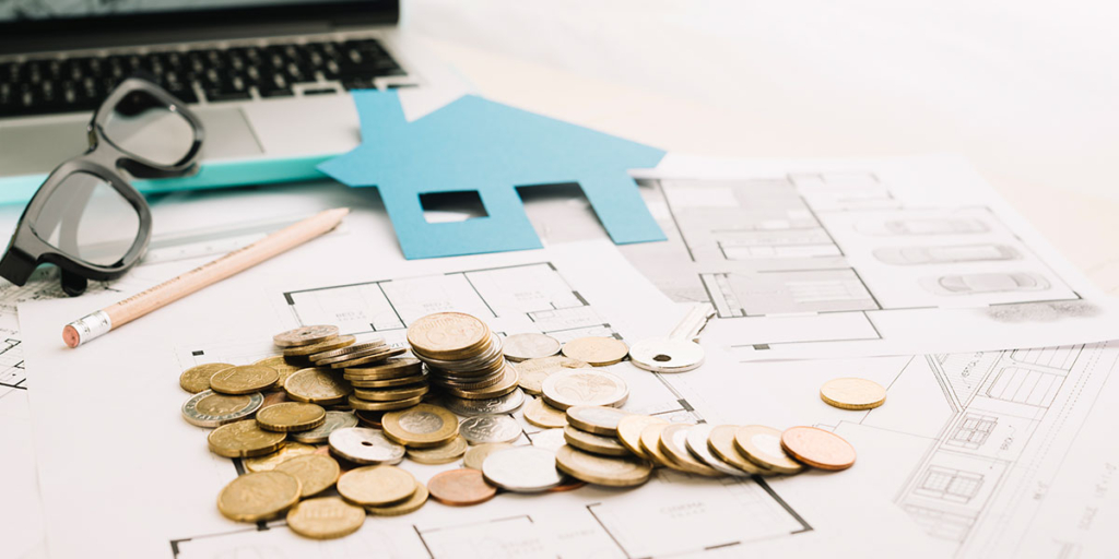Margem de lucro Margem de lucro: imagem de uma mesa com papeis de planta de imóvel com algumas moedas amontoadas em cima.