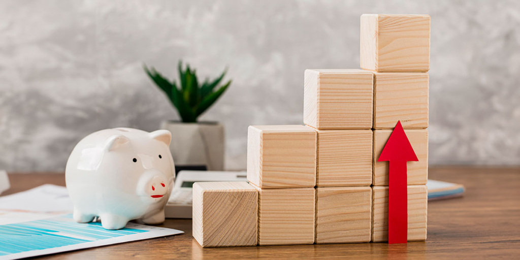 Margem de lucro Margem de lucro: imagem de um cofre em formato de porco ao lado de blocos de madeira formando uma escada e uma seta para cima.