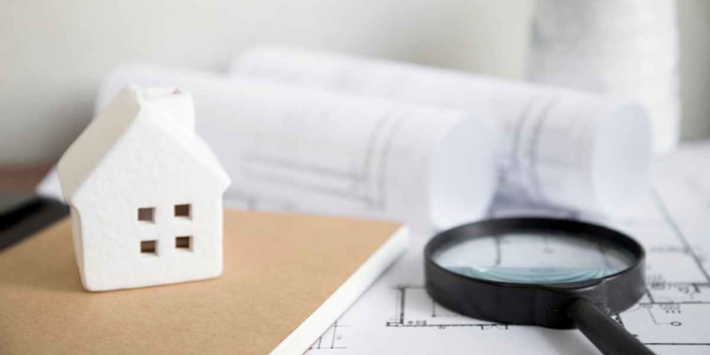 Avaliação de imóveis Avaliação de imóveis: imagem de uma mesa com alguns papeis de planta de imóvel, uma casa em miniatura e uma lupa.