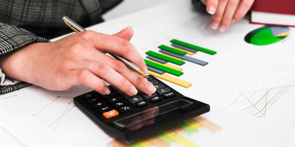 Avaliação de imóveis Avaliação de imóveis: close nas mãos de uma pessoa usando uma calculadora. Ao lado da calculadora alguns papeis com gráficos.