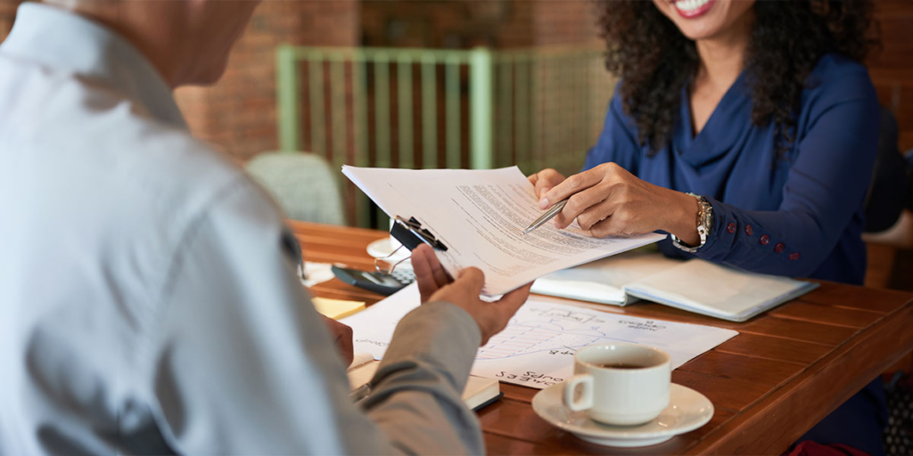 Cláusula resolutiva Cláusula resolutiva: duas pessoas numa mesa. Uma delas entrega um papel para a outra e aponta, com uma caneta, para um lugar do papel.