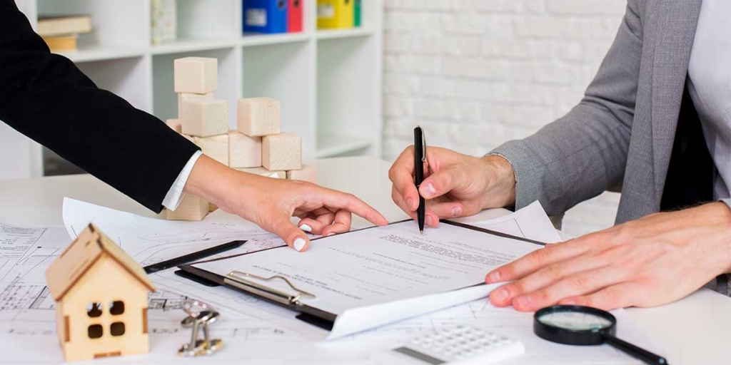 Cláusula resolutiva Cláusula resolutiva: close nas mãos de duas pessoas em cima de uma mesa. Uma delas assina um papel, a outra sinaliza onde assinar.