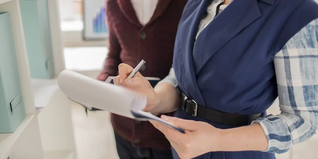 Como saber se o habite-se foi aprovado Como saber se o habite-se foi aprovado: close nas mãos de duas pessoas segurando papeis e fazendo anotações.