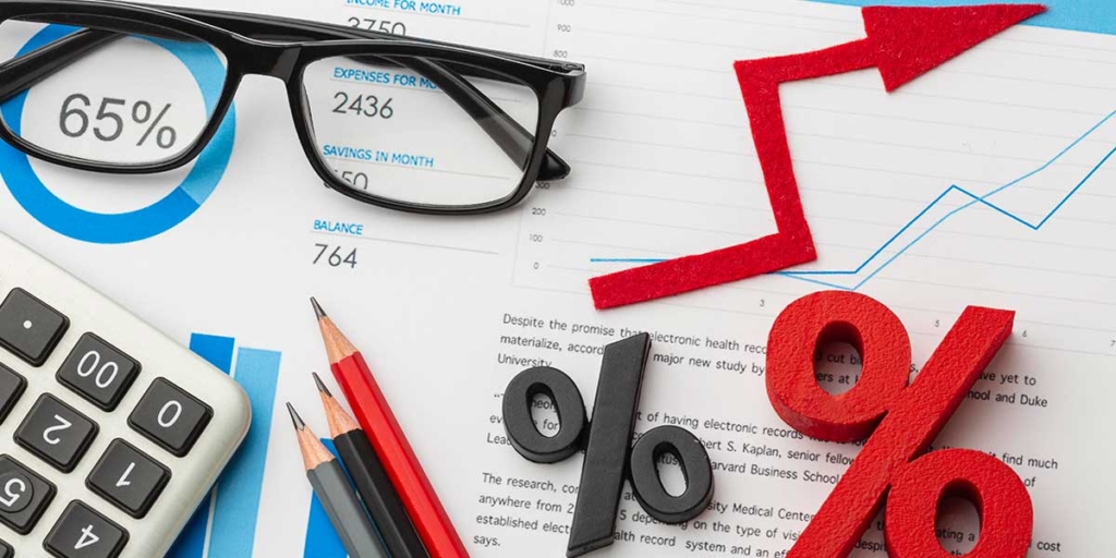 IGPM IGPM: imagem de um óculos de grau, alguns lápis, uma calculadora e alguns ícones de porcentagem em cima de alguns papeis com gráficos, números e textos.