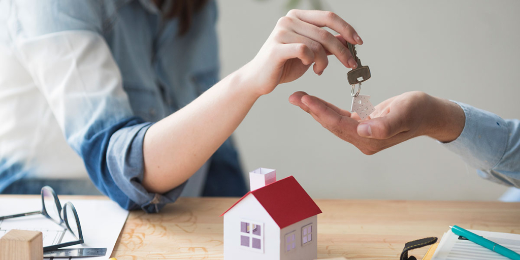 Tipos de imóveis Tipos de imóveis: close nas mãos de duas pessoas. Uma entregando uma chave a outra. Abaixo uma mesa com a miniatura de uma casa.