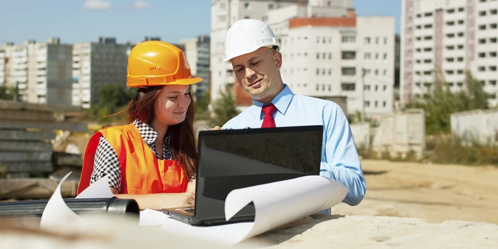 ABNT da Construção Civil ABNT da Construção Civil: imagem de um homem e uma mulher conversando num canteiro de obras. Os dois usam capacete e estão olhando para a tela de um notebook.