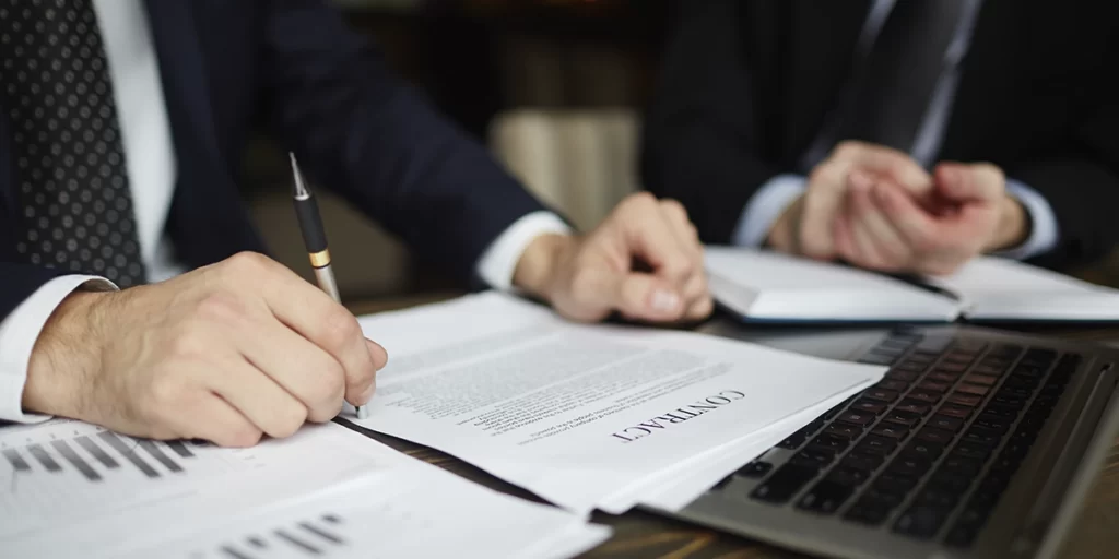 Distrato ou rescisão Distrato ou rescisão: imagem de uma mesa. Foco nas mãos de duas pessoas que usam ternos e manuseiam alguns papeis.