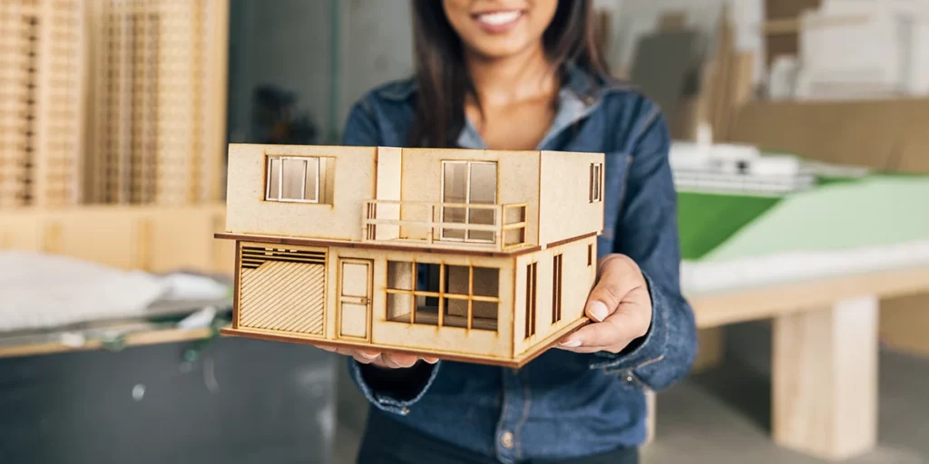 Casas Pré-fabricadas Casas Pré-fabricadas: imagem de uma mulher segurando uma maquete de madeira de um imóvel.