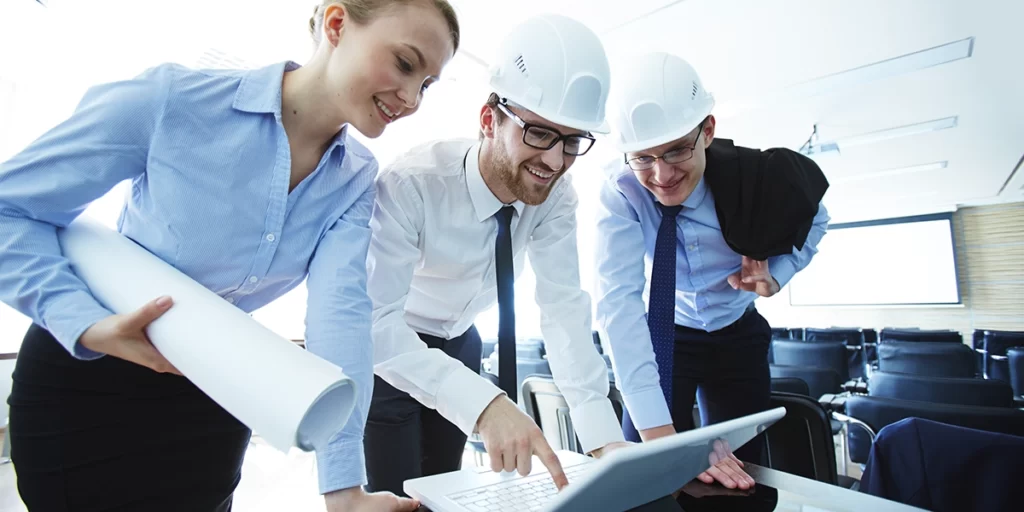 RRT RRT: imagem de dois homens e uma mulher num auditório. Os três usam ternos e estão sorrindo, olhando um notebook numa mesa.