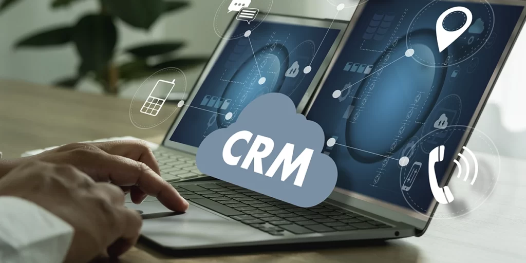 Stand de Vendas de imóveis Stand de Vendas de imóveis: close nas mãos de uma pessoa digitando num notebook. Em destaque, a sigla CRM e alguns ícones em volta.