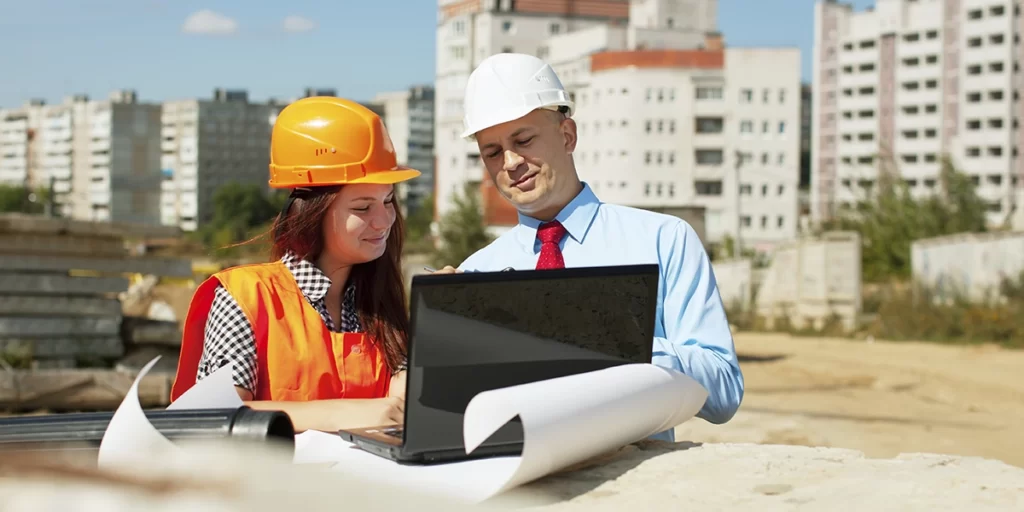 ART ART: imagem de um homem e uma mulher num canteiro de obras, usando EPI, olhando a tela de um notebook.