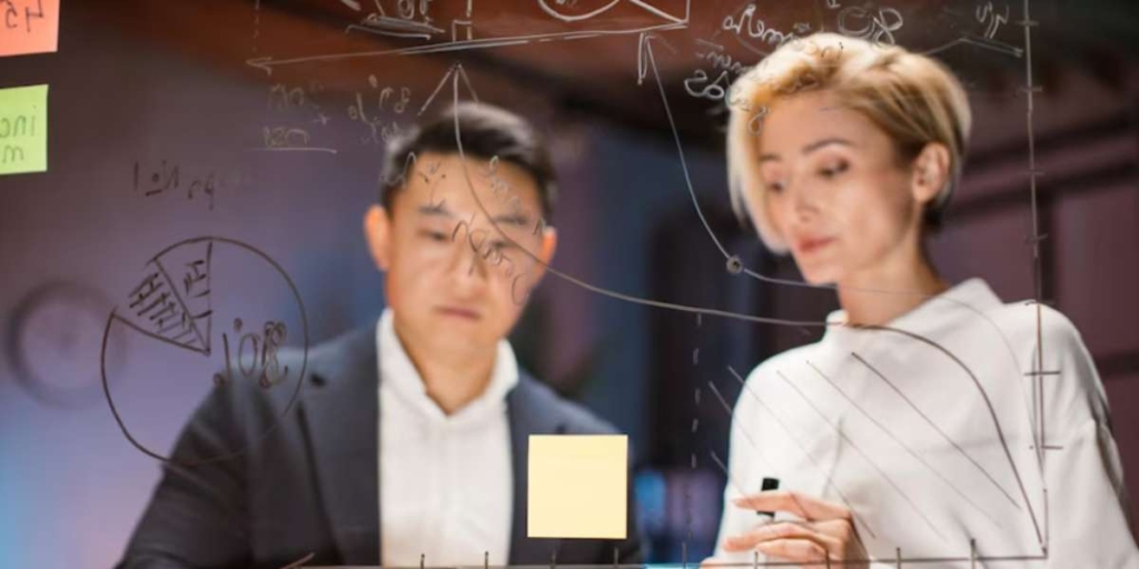 PERT/CPM PERT/CPM: imagem de duas pessoas escrevendo numa parede de vidro.