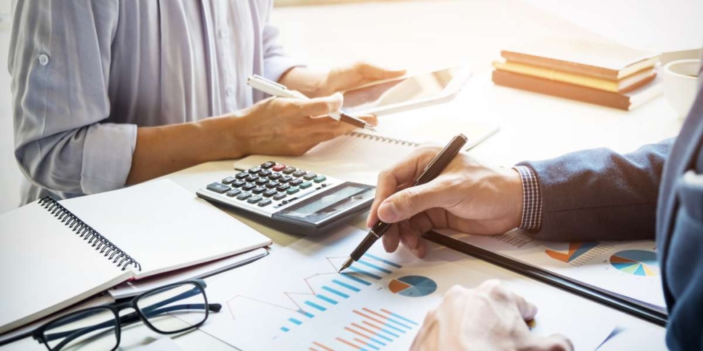 PERT/CPM PERT/CPM: close nas mãos de duas pessoas de lados opostos de uma mesa. Na mesa vemos alguns papeis com gráficos, cadernos e uma calculadora.