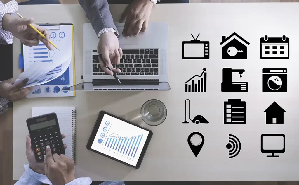 CRM imobiliario gratuito CRM imobiliario gratuito: imagem de uma mesa vista de cima. Vemos mãos de algumas pessoas interagindo. Na mesa vemos notebook, tablet, cadernos, uma calculadora. Do lado direito da imagens de vários ícones enfileirados