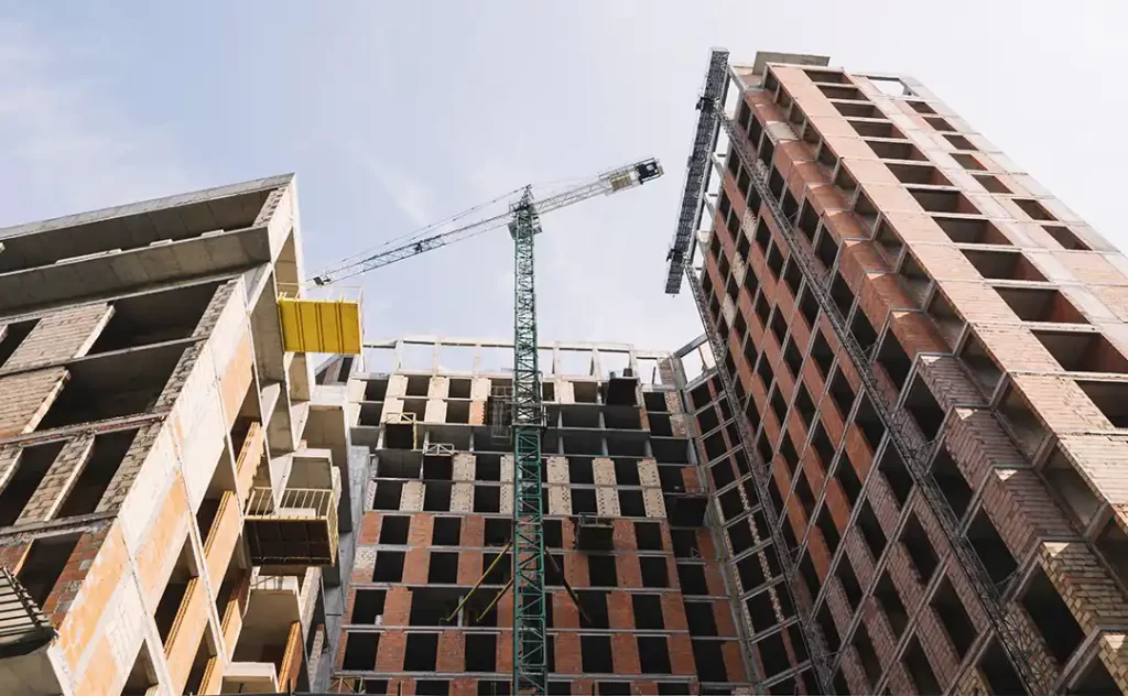 Como calcular o bdi Como calcular o bdi: A imagem mostra um edifício em construção em um ambiente urbano. Há um craneo de construção ao lado do edifício, indicando que o projeto ainda está em andamento. O edifício apresenta várias camadas de estrutura, com algumas partes ainda sem paredes, o que sugere que a construção está em um estágio avançado. O céu está claro, sugerindo um dia ensolarado.