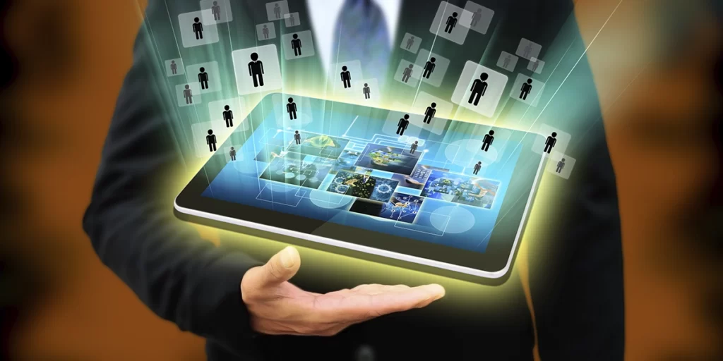 Explique como funciona o pré-atendimento Explique como funciona o pré-atendimento: A imagem mostra um homem de negócios segurando um tablet com vários ícones de mídia social saindo dele. O homem está vestido com um terno, e segura o tablet com ambas as mãos. As icônicas no tablet incluem Facebook, Twitter, LinkedIn e Instagram. O fundo é um cenário profissional com algumas luzes de escritório e sombras visíveis. A atmosfera geral da imagem é profissional e tecnológica.