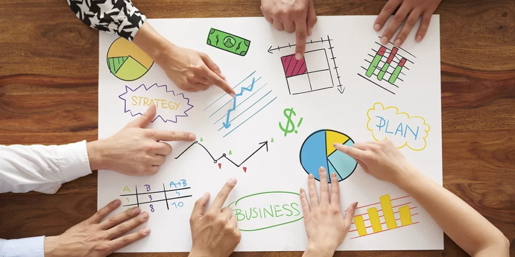 diagrama de ishikawa diagrama de ishikawa: A imagem mostra uma sessão de planejamento de negócios em andamento. Há várias mãos de pessoas segurando um papel branco sobre um tábua de madeira, com gráficos e textos que representam estratégias, planos e conceitos relacionados a negócios. Os gráficos incluem um setor de pizza, barras de gráfico, linha de tendência e outros elementos que são comuns em análises de negócios. A palavra "BUSINESS" está escrita em um quadrado verde no centro do papel, sugerindo que a sessão é sobre o desenvolvimento ou análise de estratégias para um negócio específico.