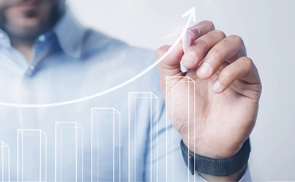 investir em lotes investir em lotes: close na mão de um homem desenhando um gráfico na tela. O gráfico está em destaque em primeiro plano na imagem. É um gráfico de barras com uma linha crescente acima.