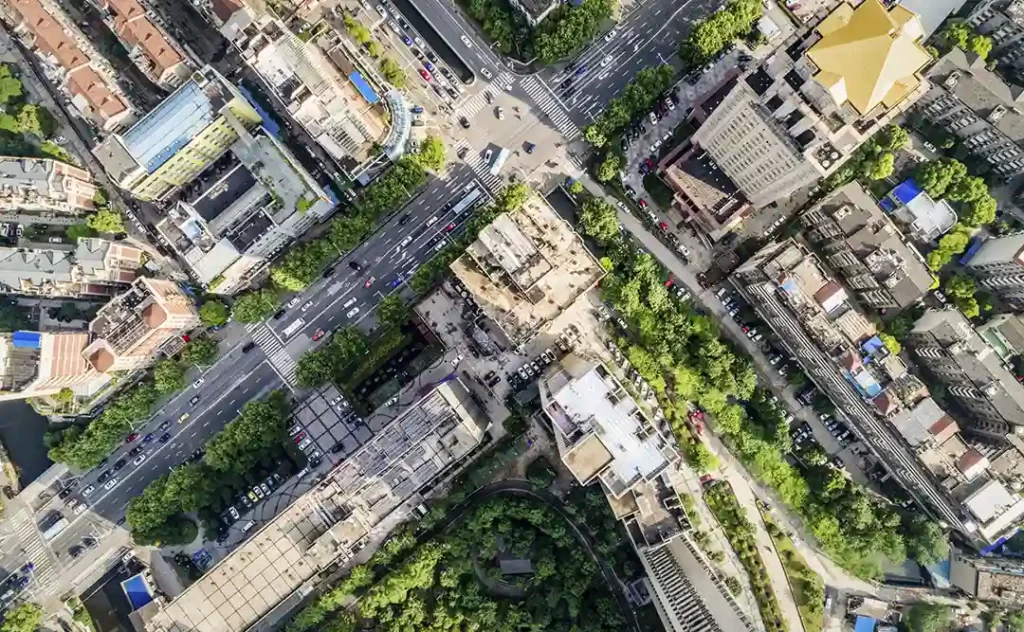 Urbanização e construção civil Urbanização e construção civil: A imagem é uma foto aérea de uma área urbana. Há uma estrutura arquitetônica complexa com edifícios de arranjo irregular, algumas de grande porte e outras de tamanho menor. Há uma estrada principal que se cruza com outra, formando um "X", e outras ruas que se bifurcam ou se cruzam. A paisagem é intercalada com áreas de vegetação, possivelmente parques ou jardins, que contrastam com o materialidade das construções. A imagem captura a densidade e a complexidade de uma cidade, com a interação entre arquitetura e espaço público.