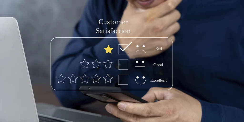 CRM na gestão de vendas de lotes CRM na gestão de vendas de lotes: A imagem mostra uma pessoa sentada diante de um laptop, com uma mão sobre o que parece ser um teclado e a outra mão usando um smartphone. O smartphone está apresentando uma interface de feedback de satisfação do cliente. A interface inclui uma barra de estrelas com uma estrela selecionada, indicando uma avaliação positiva, e três opções de feedback: "Bad" (Ruim), "Good" (Bom) e "Excellent" (Excelente), cada uma com um ícone de emoção correspondente. A imagem parece ser uma representação de uma situação comum em que um cliente fornece feedback sobre um serviço ou produto através de uma aplicação ou site.