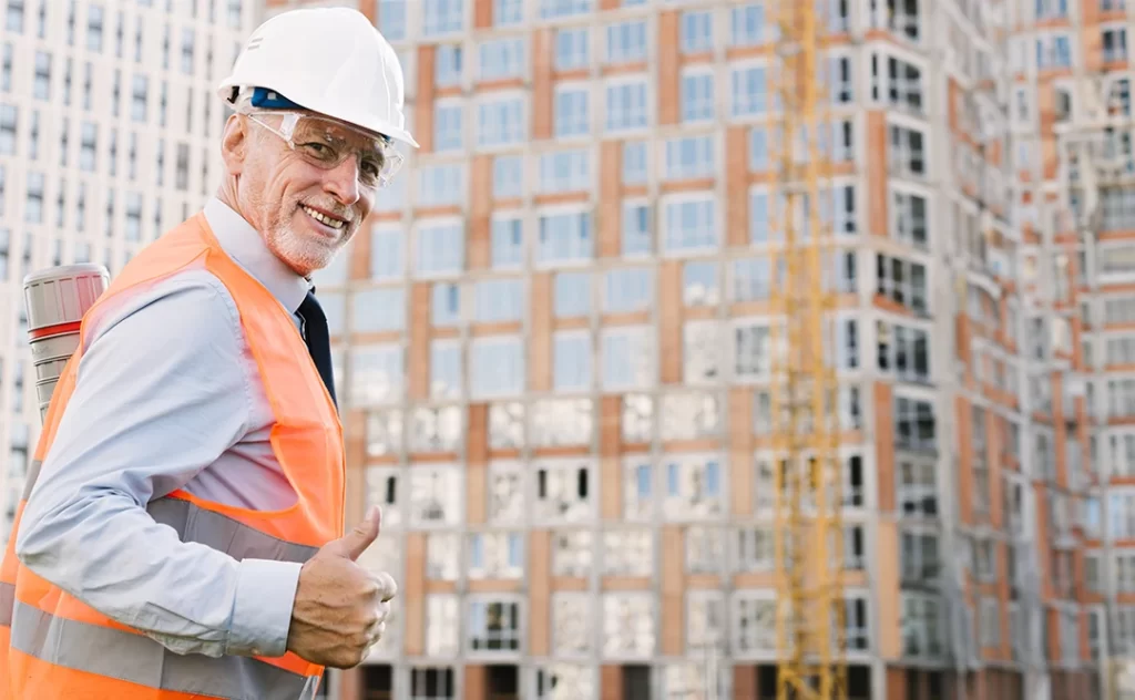 Controle de qualidade na construção civil Controle de qualidade na construção civil: A imagem mostra um homem com uma camisa de proteção e um capacete de segurança em pé diante de um local de construção com edifícios altos no fundo. Ele está dando um sinal de que tudo está bem, indicando que tudo está em ordem. A imagem é tirada de uma angulação baixa, dando a impressão de um grande local de construção com edifícios altos no fundo. O homem está vestindo uma camisa de proteção e um capacete de segurança, indicando que ele é um trabalhador de construção. A imagem é tomada durante o dia, com o sol brilhando forte no fundo. A imagem é clara e bem iluminada, sem visíveis imperfeições ou distorções.
