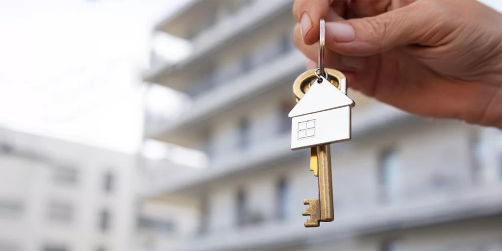 Open House Open House: A imagem mostra uma mão humana segurando uma chave de corrente. A chave tem um acabamento com um logotipo de uma casa, sugerindo que pode ser uma chave de uma casa. A chave é de cor brilhante, possivelmente metal, e está pendurada por um cabo que parece ser um corrente. A mão está na parte superior da chave, e a chave está na parte inferior da mão, indicando que a chave está sendo segurada ou mostrada. Ao fundo, há uma estrutura que parece ser um edifício, mas a foco da imagem é na chave e na mão, o que faz com que o fundo esteja desfocado e não seja possível identificar detalhes específicos do edifício.